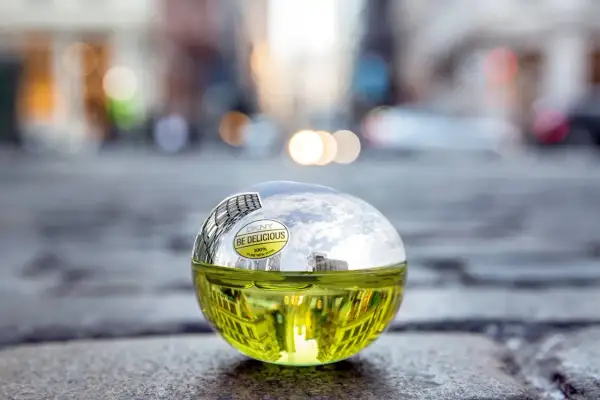 DKNY Be Delicious 100 ml, zielony flakon perfum w kształcie jabłka, odbijający miejski krajobraz.