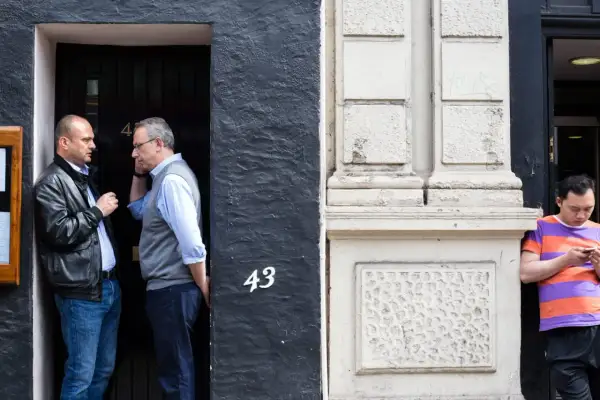 50mm street photography captures two men in conversation by a doorway numbered 43, while another man looks at his phone.