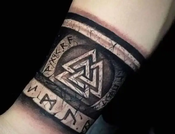 Tatuaże wikingów na przedramieniu: symbol Walhalla i runy, wyglądające jak wyryte na kamieniu.