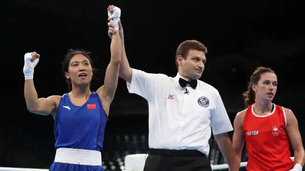 A boxer in a blue uniform with the Chinese flag raises her arm in victory as a referee holds it up. The question of what weight class is 150 in boxing is on many minds.