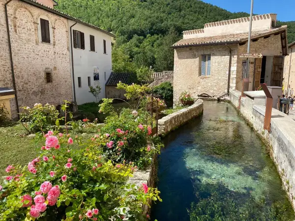 Un ruscello attraversa un borgo umbro, tra case in pietra e rose rosa. Un angolo incantevole tra i borghi più belli dell'Umbria.