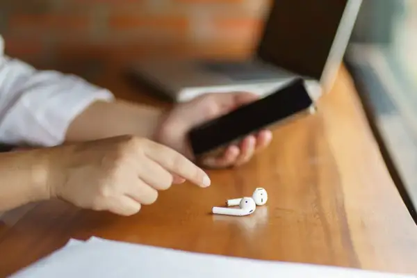 Osoba trzyma telefon, obok leżą białe słuchawki. Może to być powód, dla którego dźwięk przez Bluetooth przerywa na Androidzie.