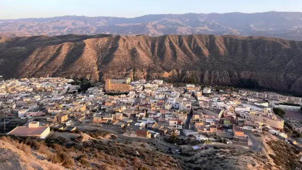 Pueblo blanco anidado en el **desierto de Tabernas**, con colinas áridas y montañas al fondo.