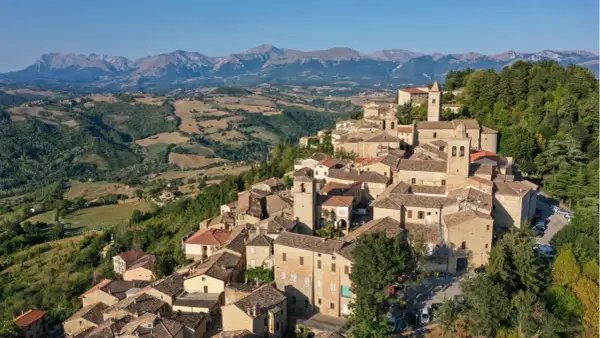 Borgo medievale di Penna San Giovanni, con le sue case in pietra e i tetti in cotto, incastonato tra dolci colline e montagne maestose.