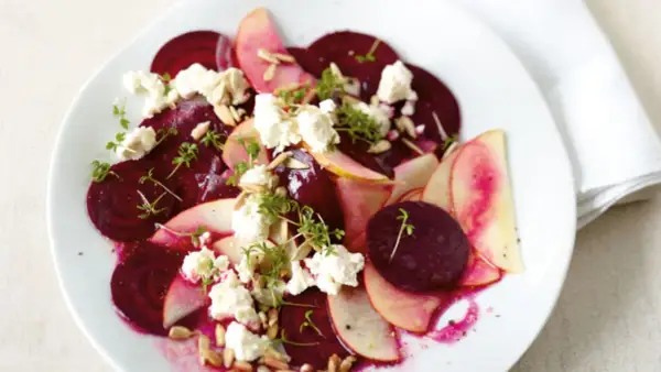 Ein köstlicher rote beete salat mit Apfelscheiben, zerbröckeltem Käse, Sonnenblumenkernen und Kresse garniert.