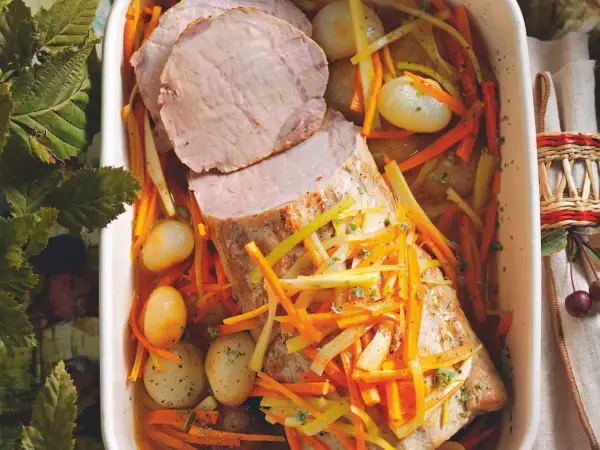 Succulento maiale in agrodolce con carote julienne, cipolline e erbe aromatiche in una teglia bianca.