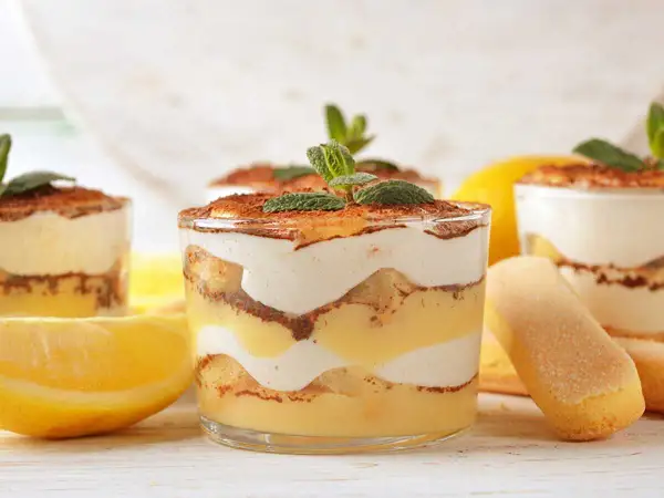 Délicieux tiramisu citron, superposé dans des verres avec des biscuits à la cuillère et des citrons frais.