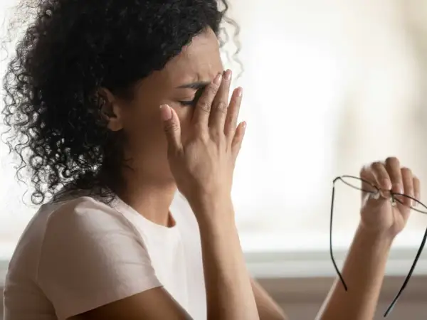 Frau reibt sich die Augen, hält Brille in der Hand. Sie fühlt sich erschöpft, vielleicht wegen **Schwindel durch Stress**.