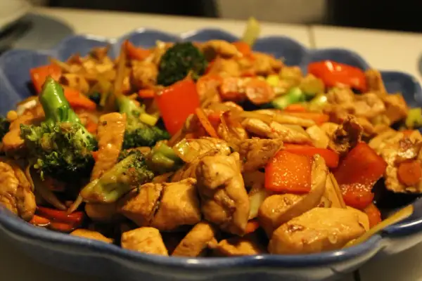 En blå skål fylld med wokad kyckling, broccoli, paprika och morötter. En läcker och färgstark måltid.