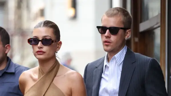 Hailey Bieber und Justin Bieber, beide mit Sonnenbrillen, wirken semi-formal. Sie spazieren durch die Stadt, sie in einem braunen Top, er im Anzug.