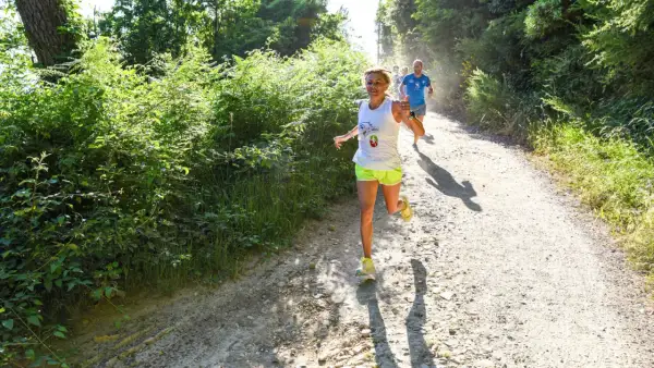 Donne e uomini corrono su un sentiero sterrato in un bosco, godendosi la corsa con il caldo estivo.
