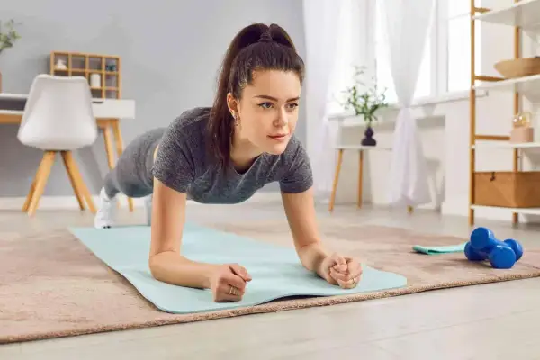 Donna in posizione di plank, parte di un allenamento metabolico casalingo. Sul tappetino, manubri blu.