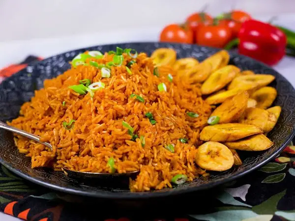 En stor portion jollof rice med stekt plantain, garnerad med salladslök. En härlig måltid!
