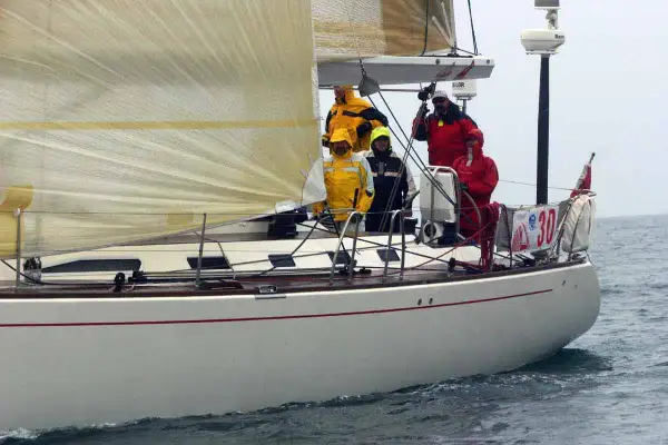 Equipaggio su una barca a vela, con un uomo che sembra D'Alema in giacca gialla.