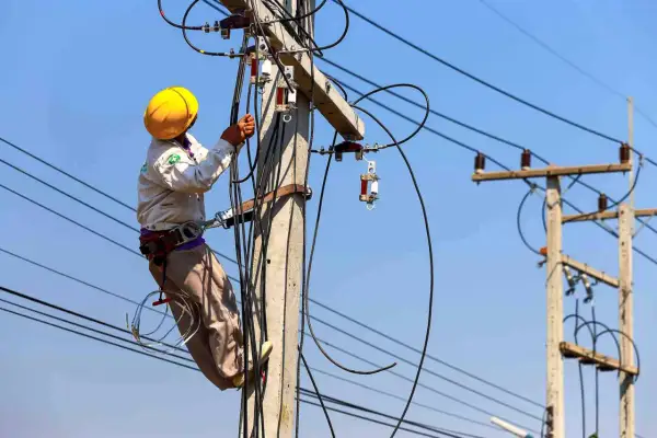 Elektryk w żółtym kasku pracuje na słupie energetycznym, podłączając kable. Zastanawiasz się, ile kosztuje przyłącze prądu?
