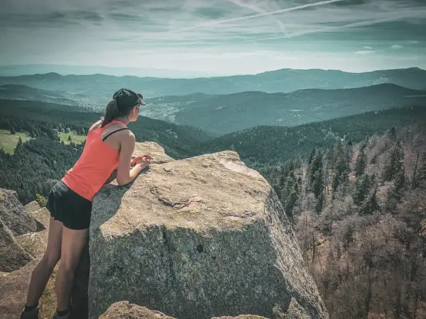 Une femme profite d'une vue panoramique sur les Vosges lors d'un trek. Les montagnes s'étendent à perte de vue sous un ciel nuageux.