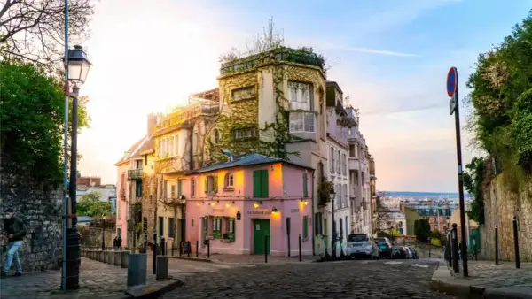 Ein malerisches Viertel in Paris, perfekt für einen Kurztrip. Ein rosa Restaurant mit grünen Fensterläden, umgeben von charmanten Häusern, lädt zum Verweilen ein.