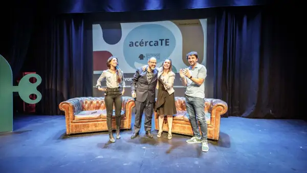 Cuatro personas celebran en un escenario con sofás y un cartel de "acércaTE". Un evento de podcast psicologia.