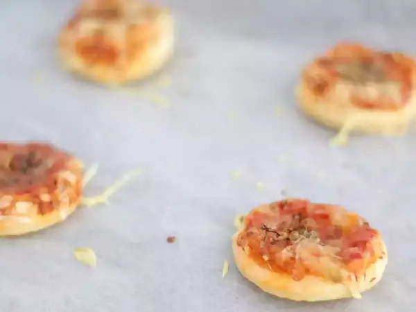 Quattro pizzette di pasta sfoglia appena sfornate, dorate e filanti, pronte per essere gustate.