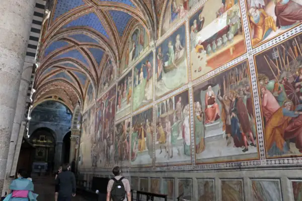 Interno del duomo di San Gimignano con affreschi medievali e volte blu stellate.