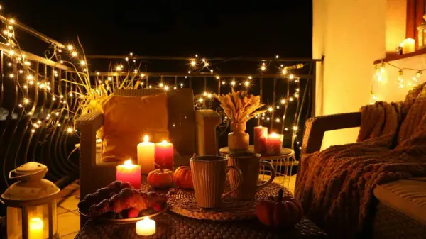 Przytulny balkon z jesienne dekoracje diy: migoczące lampki, dynie, świece i gorące napoje.
