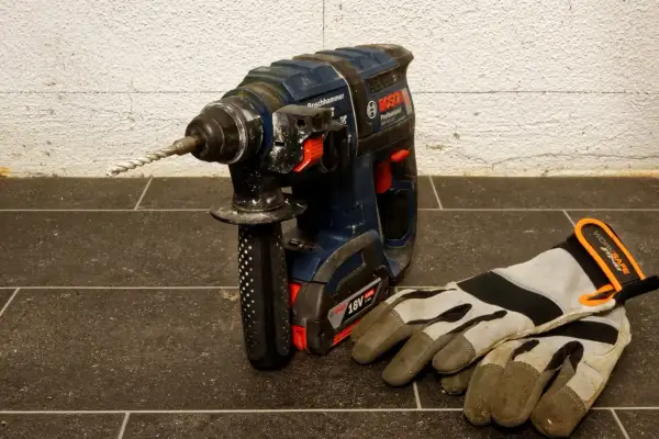Mocna wiertarka udarowa Bosch z zamontowanym wiertłem i rękawicami roboczymi obok. Dowiedz się, jak wyjąć wiertło z wiertarki.