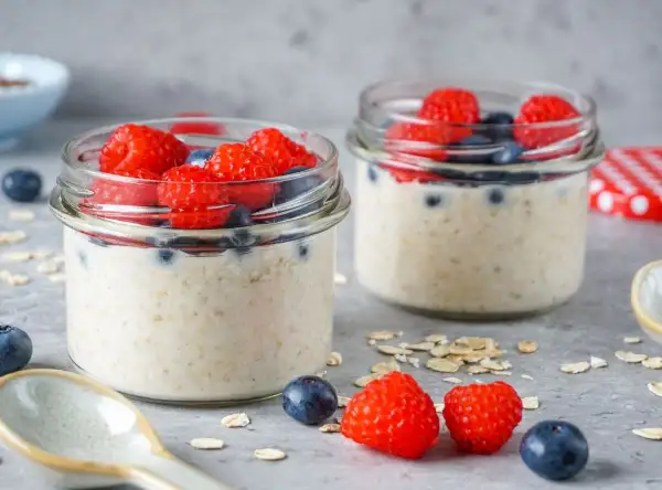 Zwei Gläser mit Overnight Oats, garniert mit Himbeeren und Blaubeeren. Perfekt für gesunde Overnight Oats Rezepte.