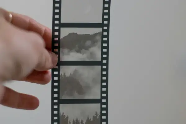 Dłoń trzyma kadr z taśmy filmowej, ukazujący mgliste góry i lasy.