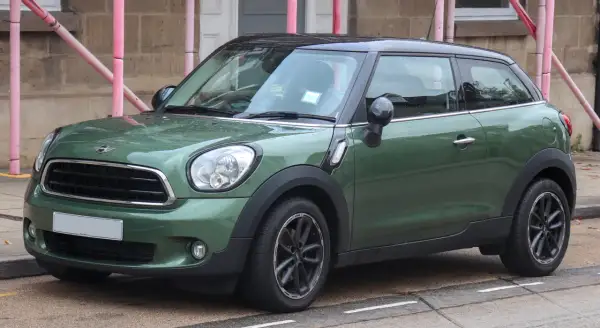Zielony mini paceman z czarnym dachem stoi na ulicy, mokry od deszczu.