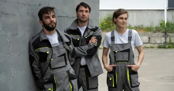 Trzech pracowników w szarych kombinezonach z neonowymi akcentami. Polski producent odzieży roboczej prezentuje nowoczesne ubrania.