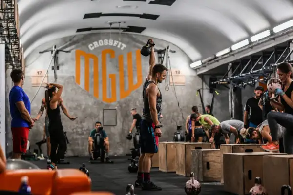 Ludzie ćwiczący CrossFit w siłowni, jeden mężczyzna podnosi kettlebell.