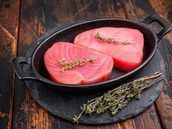 Deux beaux pavés de thon rouge cru, ornés de brins de thym frais, prêts pour une recette savoureuse.
