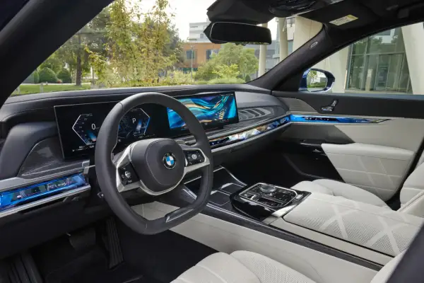 Wnętrze BMW 740d z nowoczesnym panelem cyfrowym, podświetlanymi detalami i komfortowymi, białymi fotelami.