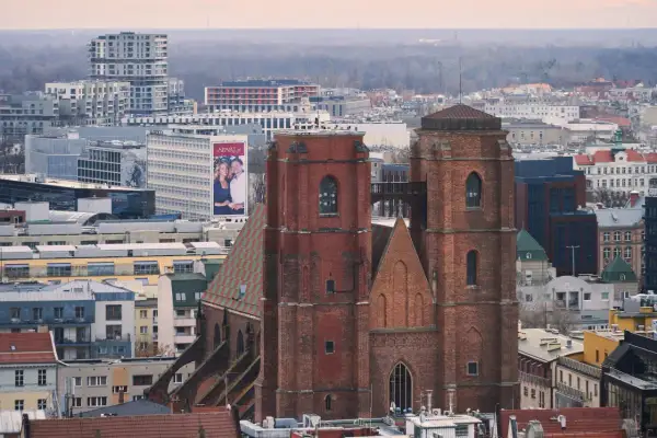 Widok na ceglany kościół garnizonowy we Wrocławiu, otoczony nowoczesną zabudową miejską.