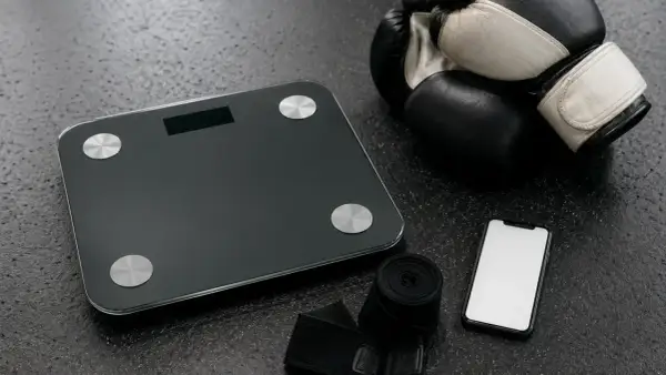 Boxing gloves, hand wraps, a scale, and a smartphone are laid out, ready for an amateur boxer to check their weight for the correct amatuer boxing weight classes.