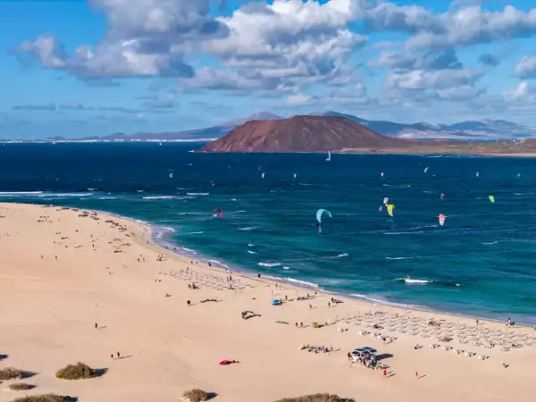 Fuerteventura, gdzie najlepiej? Plaża z kitesurferami i turystami, w tle wulkan i góry. Idealne miejsce na wakacje.