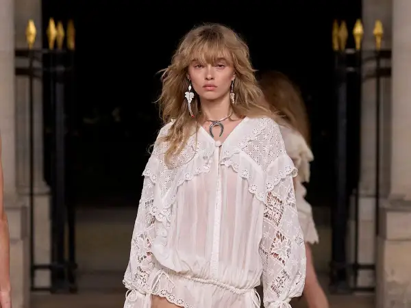 Modelo luce un vestido blanco con encaje, estilo boho, con pendientes largos y collar plateado.