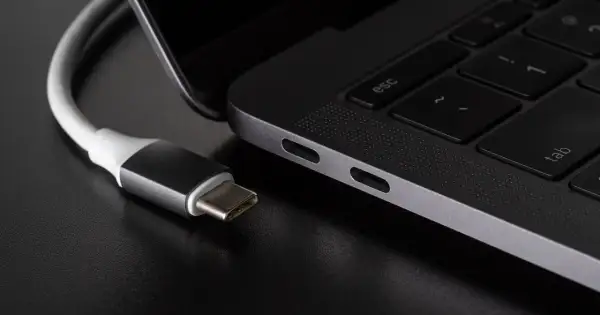 Kabel USB C zbliża się do portu laptopa. Widać jego metalową wtyczkę i biały kabel.