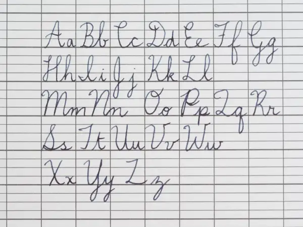 The alphabet in cursive, from A to Z, is written in neat blue ink on lined paper. The handwriting is perfect in cursive, showing each letter's formation.