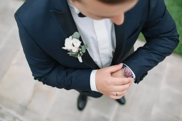 Elegancka butonierka dla pana młodego i świadka, ozdobiona białymi kwiatami i zielonymi liśćmi, dodaje szyku granatowemu garniturowi.