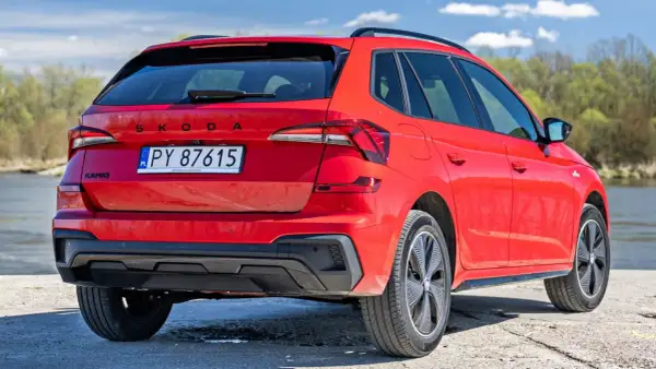 Czerwona Skoda Kamiq z polskimi tablicami rejestracyjnymi, zaparkowana nad wodą. Sprawdź atrakcyjną skoda kamiq cena!