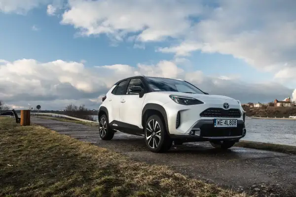 Biały Toyota Cross Yaris zaparkowany nad rzeką, z chmurami na niebie.