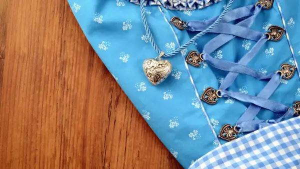 Ein Dirndl-Mieder mit Herzanhänger und Schnürung liegt auf Holz. Bald wird die Dirndlschürze gewaschen.