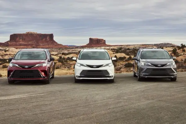 Trzy samochody Toyota Sienna w kolorach: wiśniowym, białym i grafitowym, stoją na tle pustynnego krajobrazu z formacjami skalnymi.