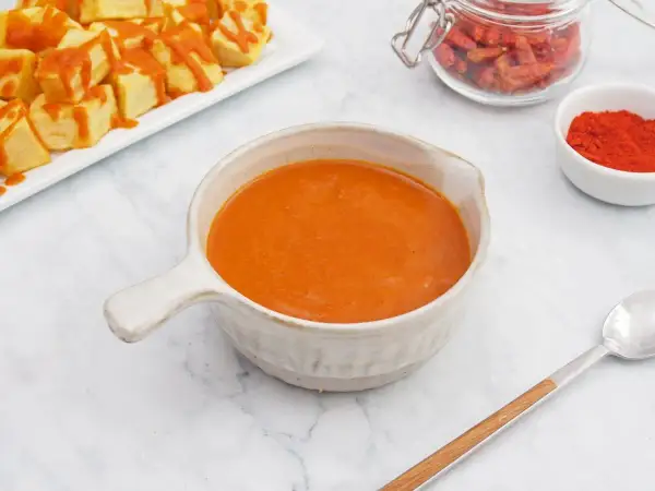 Un cuenco de cremosa salsa brava, lista para acompañar unas patatas. En el fondo, pimentón y guindillas secas.