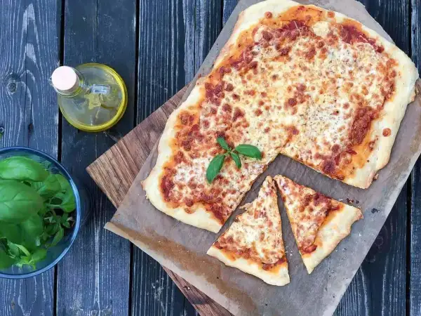 Pyszna margarita pizza z roztopionym serem i bazylią, obok oliwa i świeże liście.