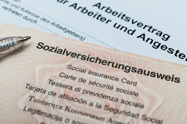Sozialversicherungsausweis zeigt, wo man die Sozialversicherungsnummer findet. Ein Arbeitsvertrag liegt daneben.
