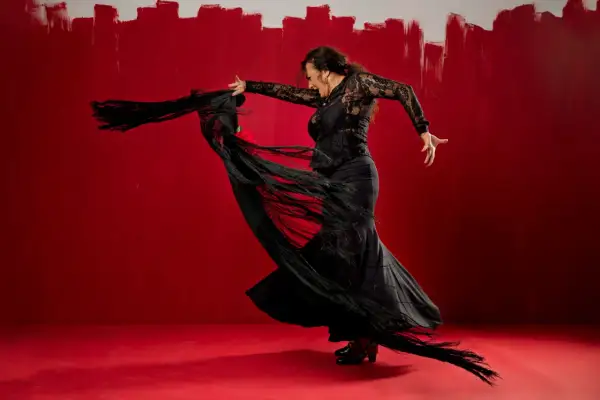 Bailarina de flamenco con mantón negro sobre fondo rojo vibrante.