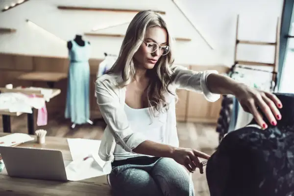 Eine Designerin mit Brille misst Stoff für ihr nächstes Projekt im Bereich IU Modemanagement.