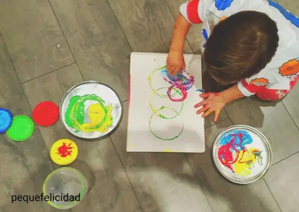 Niño pequeño creando arte con pintura de dedos. Lienzo con círculos de colores y recipientes de pintura.